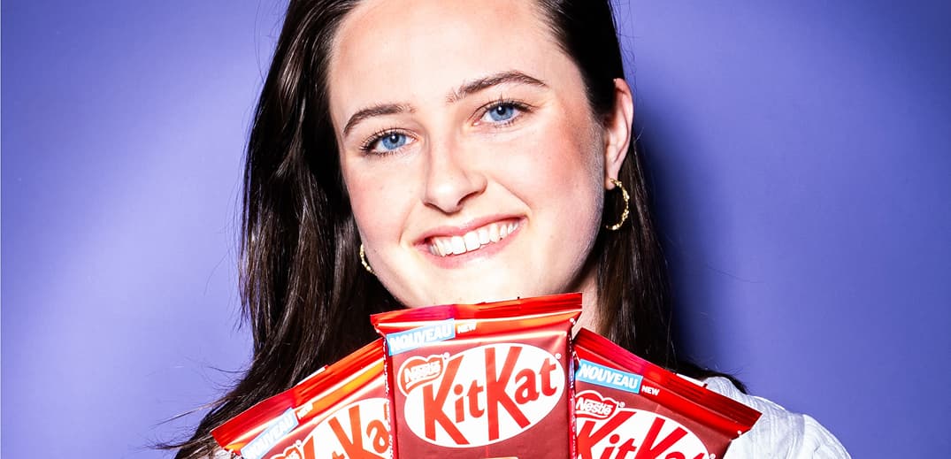 A person holds multiple KitKat chocolate bars in front of a purple background.